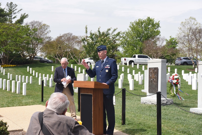A man standing in a cemetery speaks to a seated crowd.
