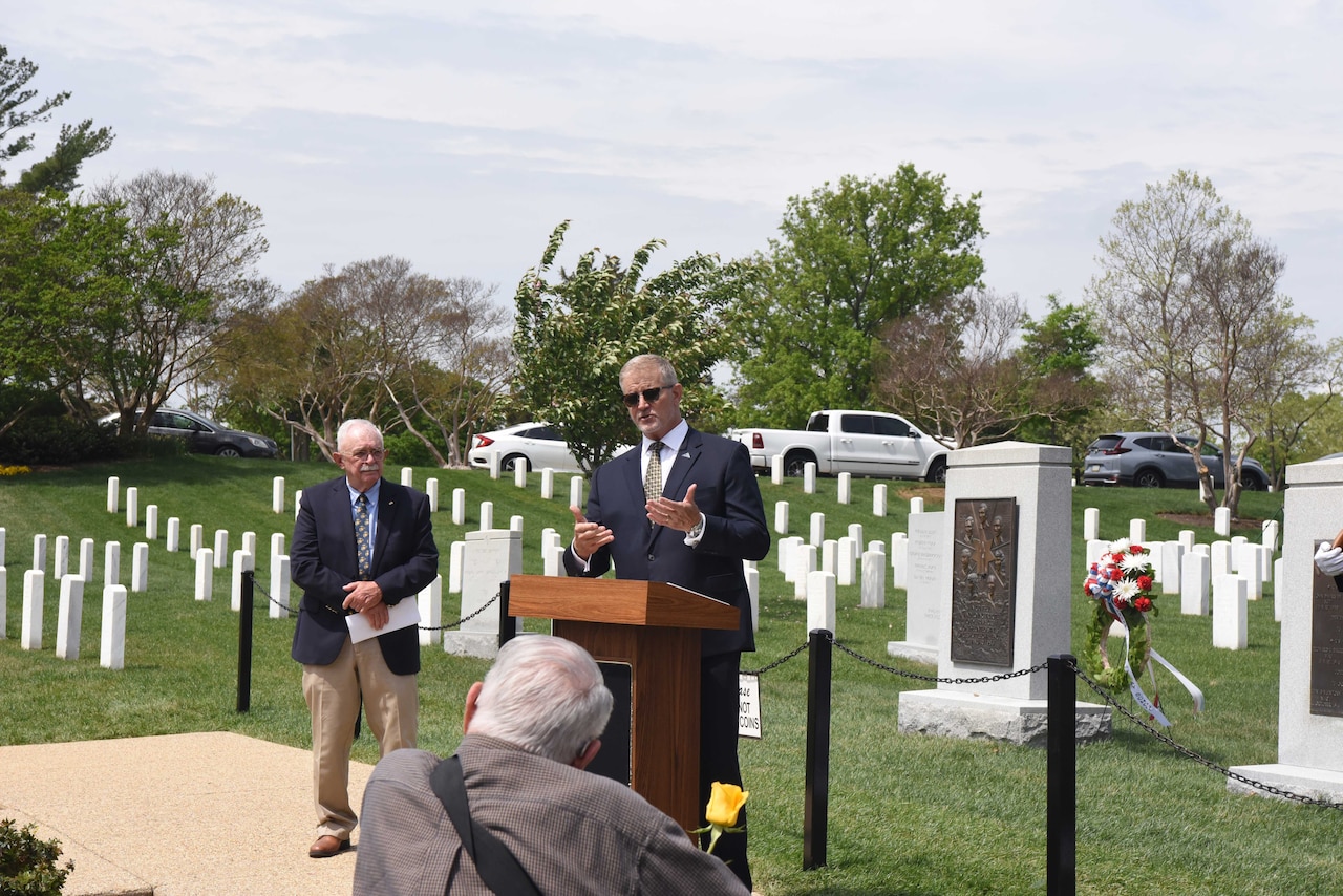 A man standing in a cemetery speaks to a seated crowd.