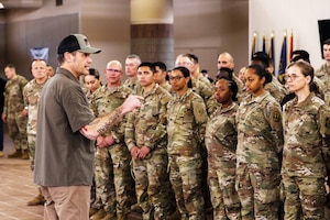 A man stands in front of more than a dozen uniformed individuals.