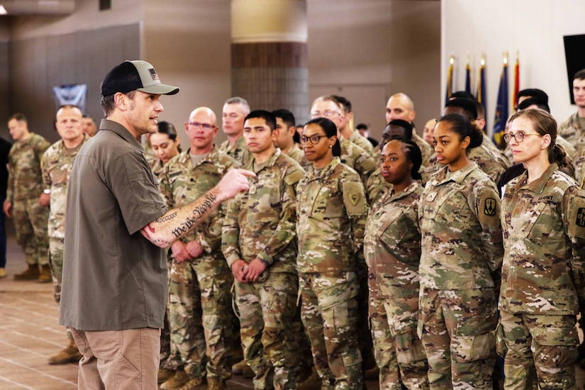 A man stands in front of more than a dozen uniformed individuals.