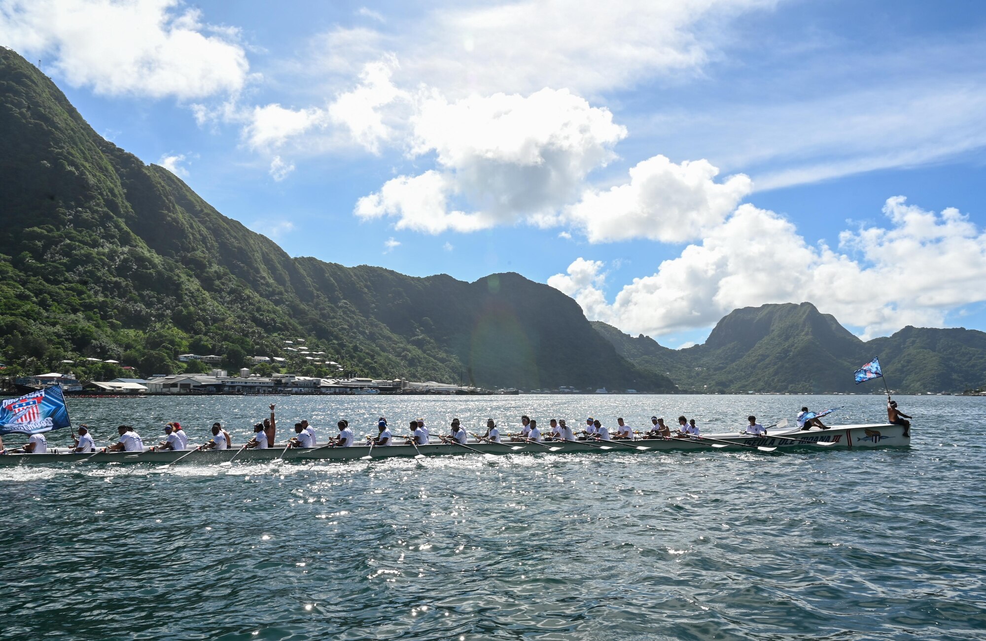 A fautasi team sails past after completing an early round of the race in Pago Pago, American Samoa, April 16, 2025. Flag bearers raised their team flag proudly at each end of the boat, honoring the village they represented. (U.S. Air Force photo by Senior Airman Melody Bordeaux)