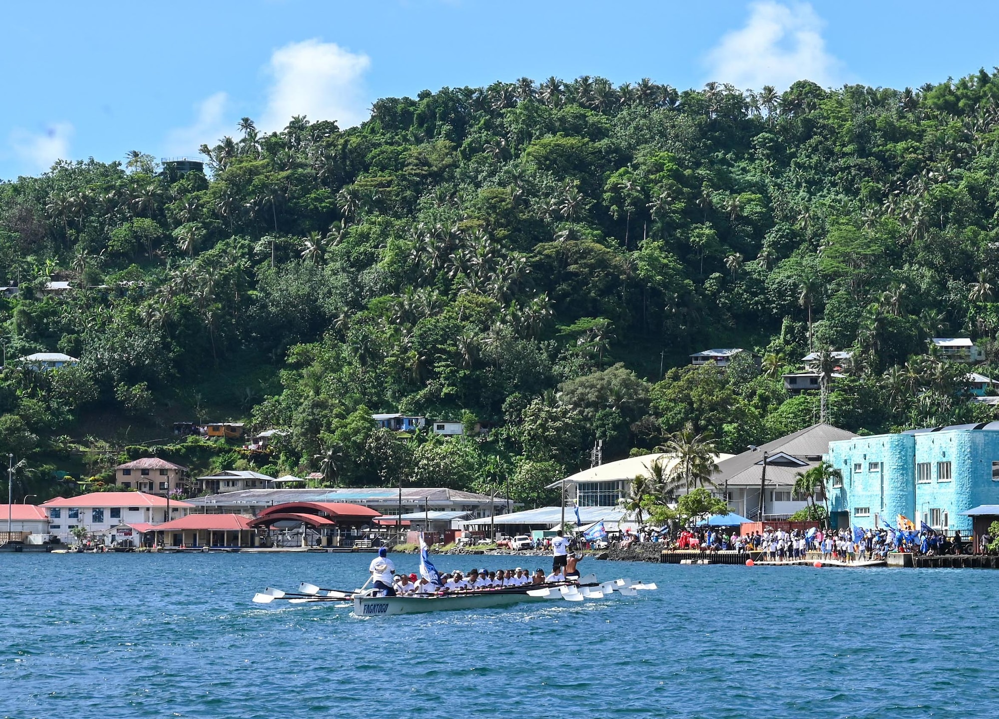 A fautasi team sails past cheering supporters after completing an early round of the race in Pago Pago, American Samoa, April 16, 2025. Supporters waved team flags and the moment captured the close-knit bond between the crews and their communities, united in effort and spirit. (U.S. Air Force photo by Senior Airman Melody Bordeaux)