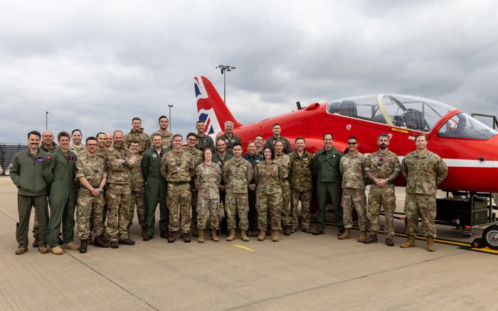 uniformed U.S., U.K., an Australian military members of C2WAC 25-3 stand in front of a Red Arrow Hawk T1
