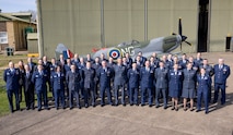 uniformed U.S., U.K., an Australian military members stand in front of Battle of Britian Memorial Flight hangar