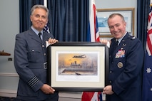 uniformed Royal Air Force and U.S. Air Force military members stand holding a frame picture.