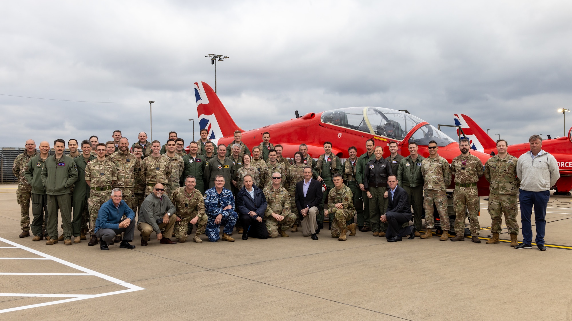 uniformed C2WAC 25-3 students from U.S., U.K., and Australian military members along with 705th Training Squadron cadre, U.S. military, civilians and contractors, stand in front of a Red Arrow Hawk T1