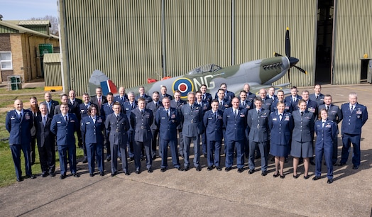  uniformed U.S., U.K., an Australian military members stand in front of Battle of Britian Memorial Flight hangar