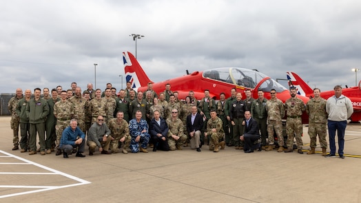  uniformed C2WAC 25-3 students from U.S., U.K., and Australian military members along with 705th Training Squadron cadre, U.S. military, civilians and contractors, stand in front of a Red Arrow Hawk T1
