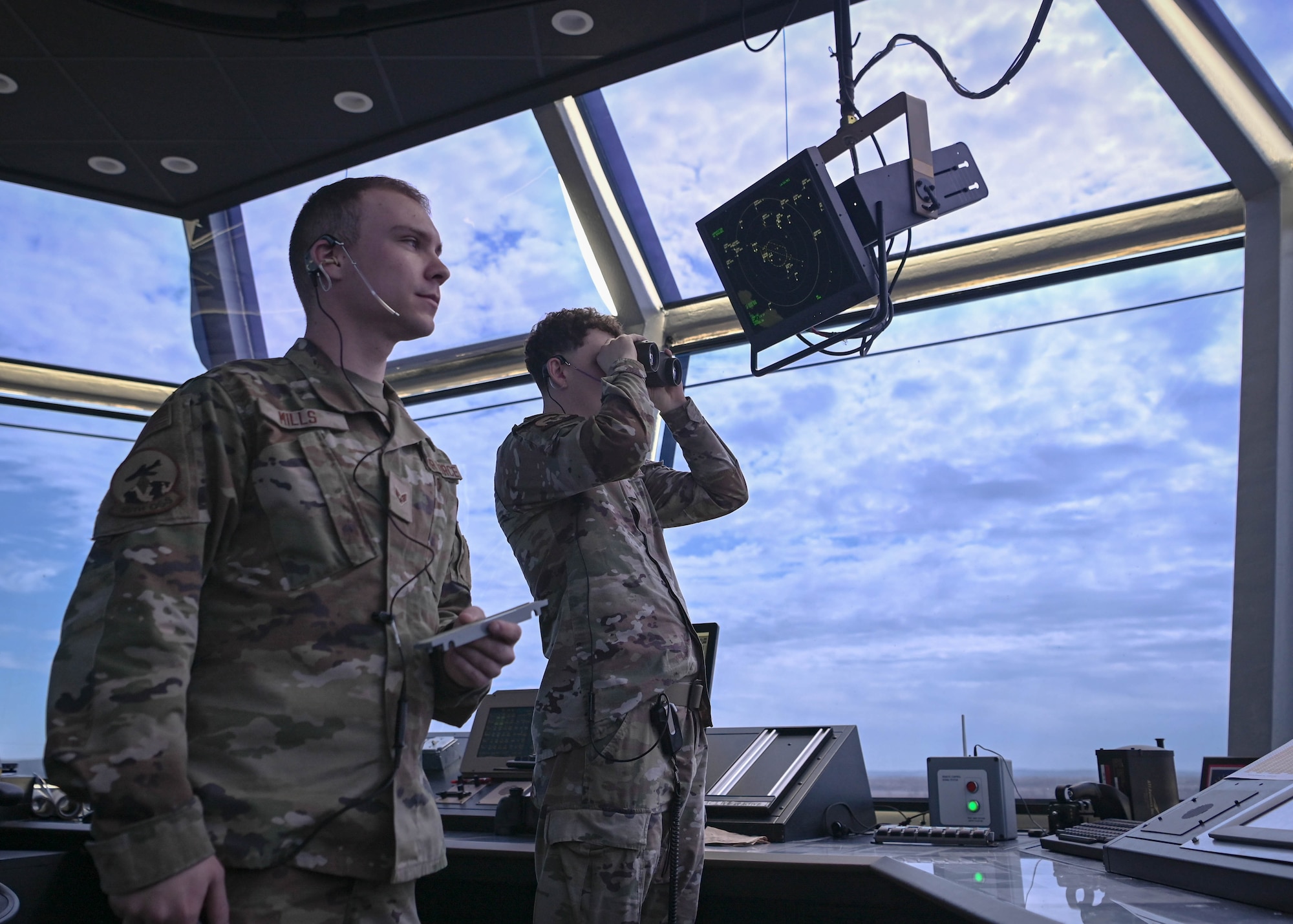 Senior Airman Daniel Mills, 55th Operations Support Squadron air traffic control trainer, and Airman 1st Class Jacob Paulus, 55th OSS air traffic controller, observe the Offutt runway from the air traffic control tower cab March 26, 2025. Air traffic controllers ensure the airspace and airfield are safe for pilots to navigate to and from. (U.S. Air Force photo by Daniel Martinez)