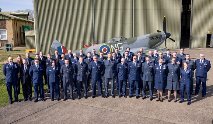 uniformed U.S., U.K., an Australian military members stand in front of Battle of Britian Memorial Flight hangar