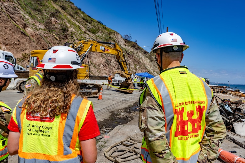 Two people in vests and hardhats observe a debris removal operations site