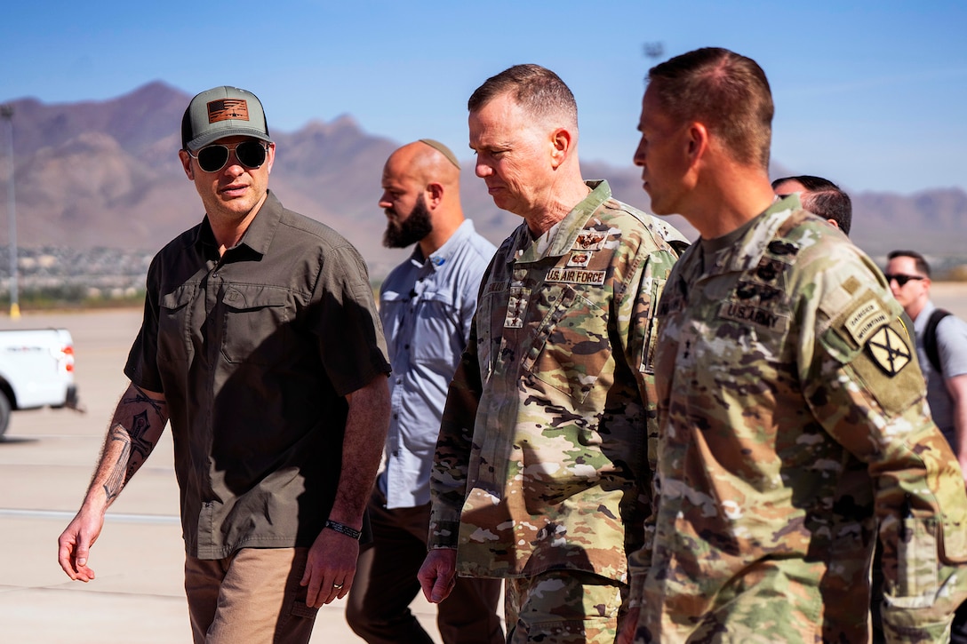 Three leaders walk side by side with mountains in the background.