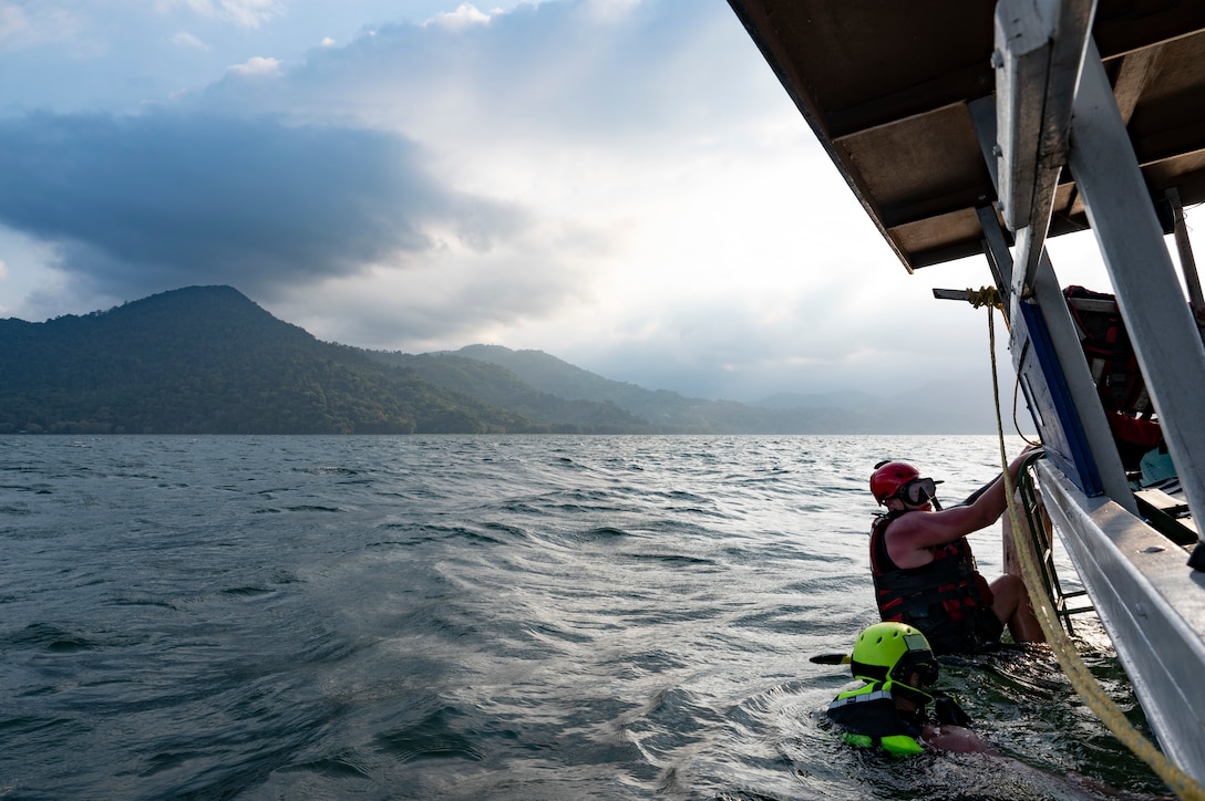 U.S. Army 1st Sgt. Peter Knope, top, climbs into a boat while Staff Sgt. James Fernald, 1st Battalion, 228th Aviation Regiment Joint Task Force-Bravo critical care flight paramedics, wades in the water, at the end of a simulated overwater hoist rescue at Lake Yojoa, Honduras, April 23, 2025. The 1-228th AB partnered with the local Honduran boatsman to conduct the two-day event to ensure members could safely hone their emergency medical skills and be prepared to rescue if the occasion arose. (U.S. Air Force photo by Staff Sgt. Sadie Colbert)