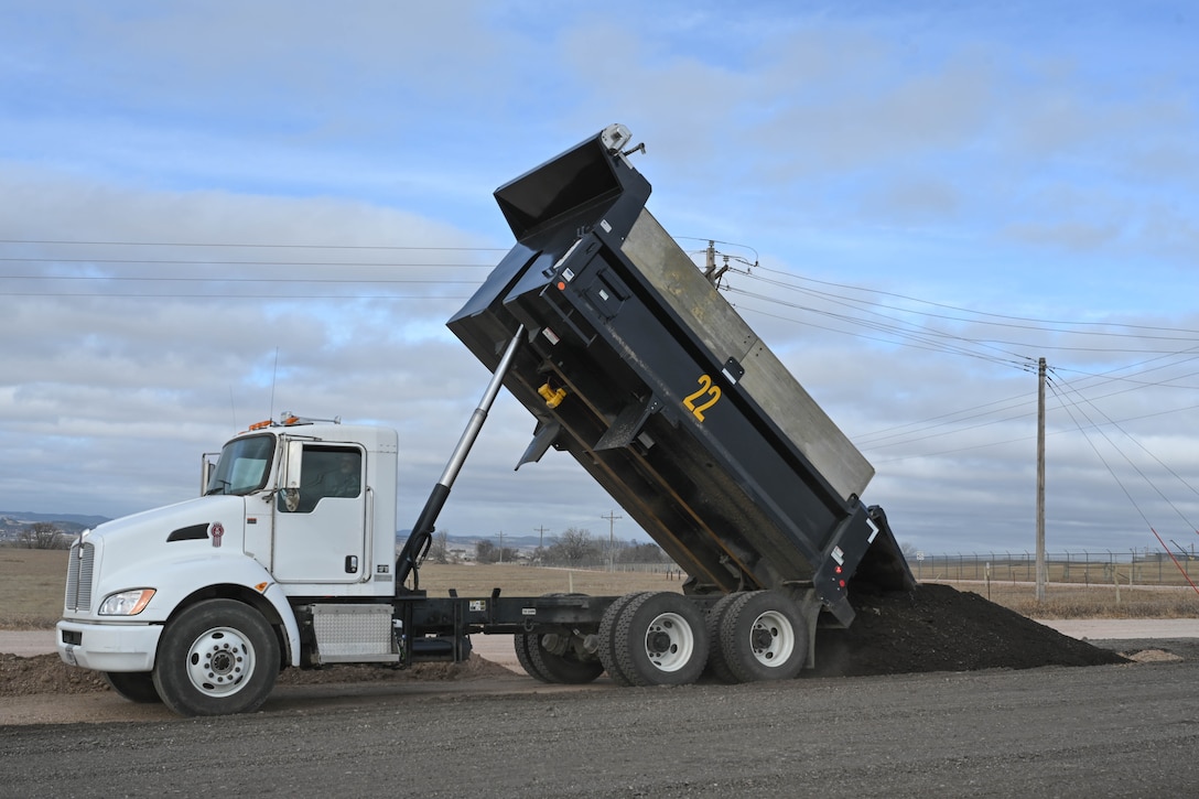 A dump truck unloads crushed asphalt.