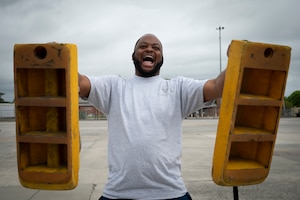 A man wearing a t-shirt holds a large yellow block in each hand