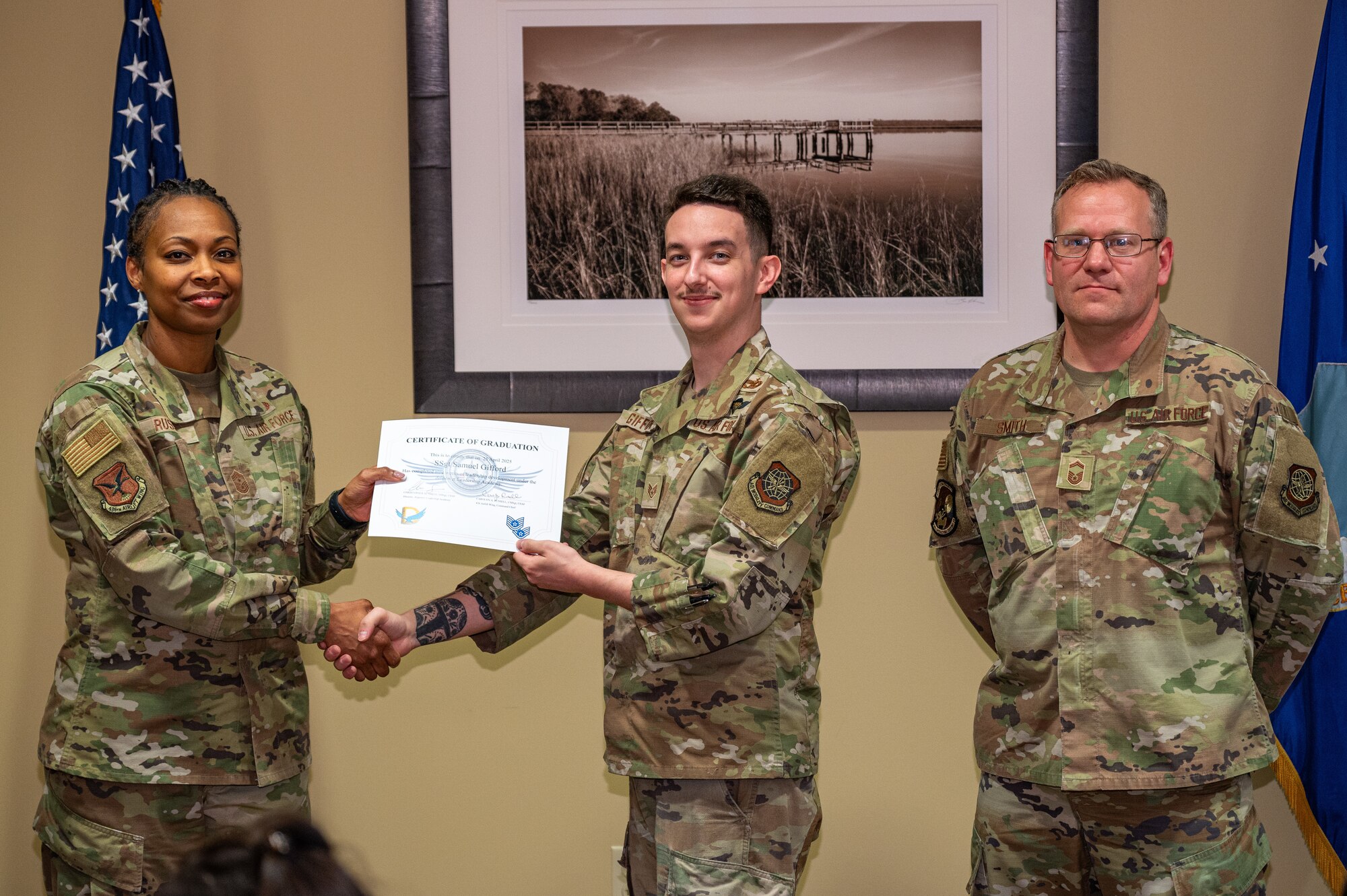 An Airman receives a certificate and and does a shake and take while posing for photo.