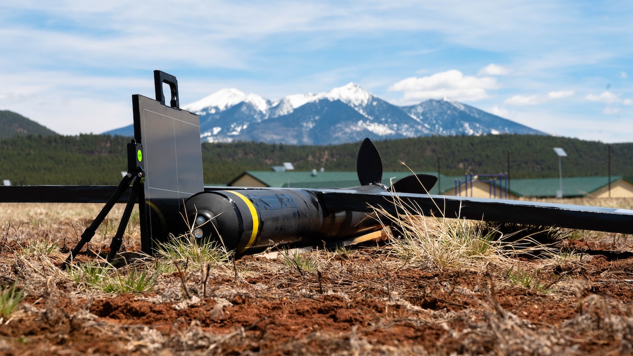 A mock unmanned aerial system with simulated explosives (center) and a new X-ray system (left) are staged on a field during an exercise.