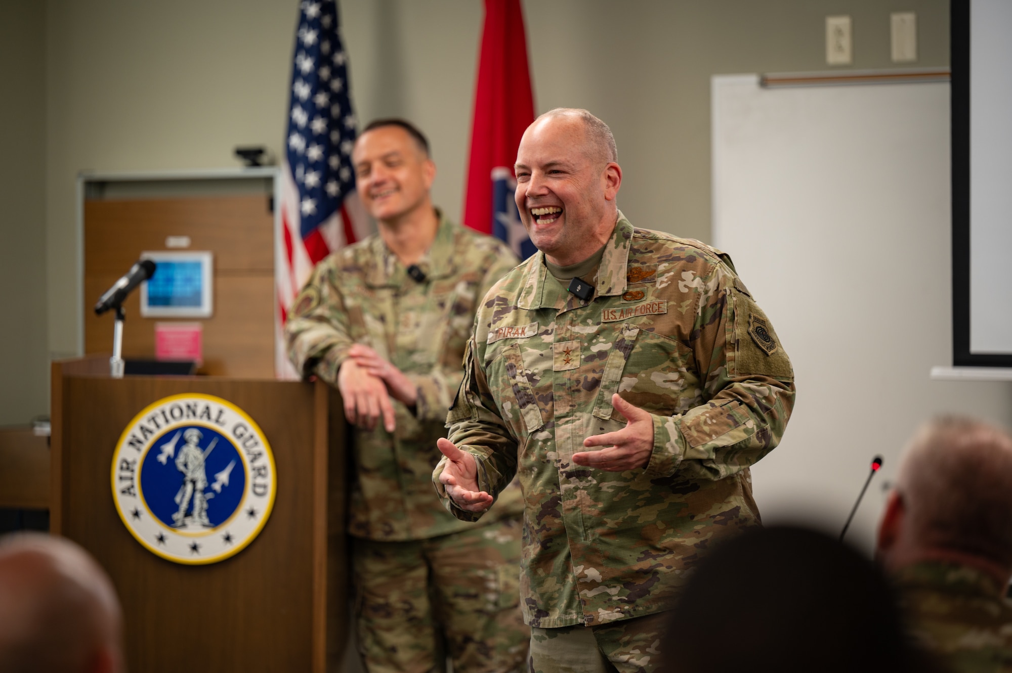 A uniformed service member is is seen behind the backs of audience member's heads while laughing.