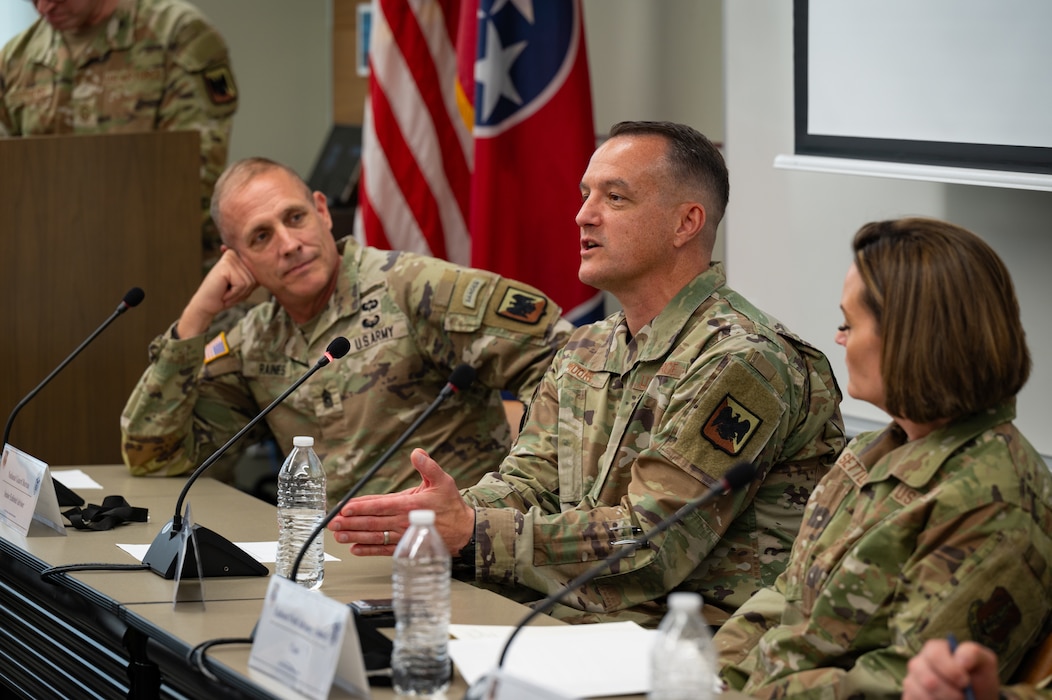 An Airman in an OCP-patterned military uniform is seen on a panel of other uniformed service members speaking into a microphone.

leans into a microphone and gestures with his hand while answers a question on a panel.