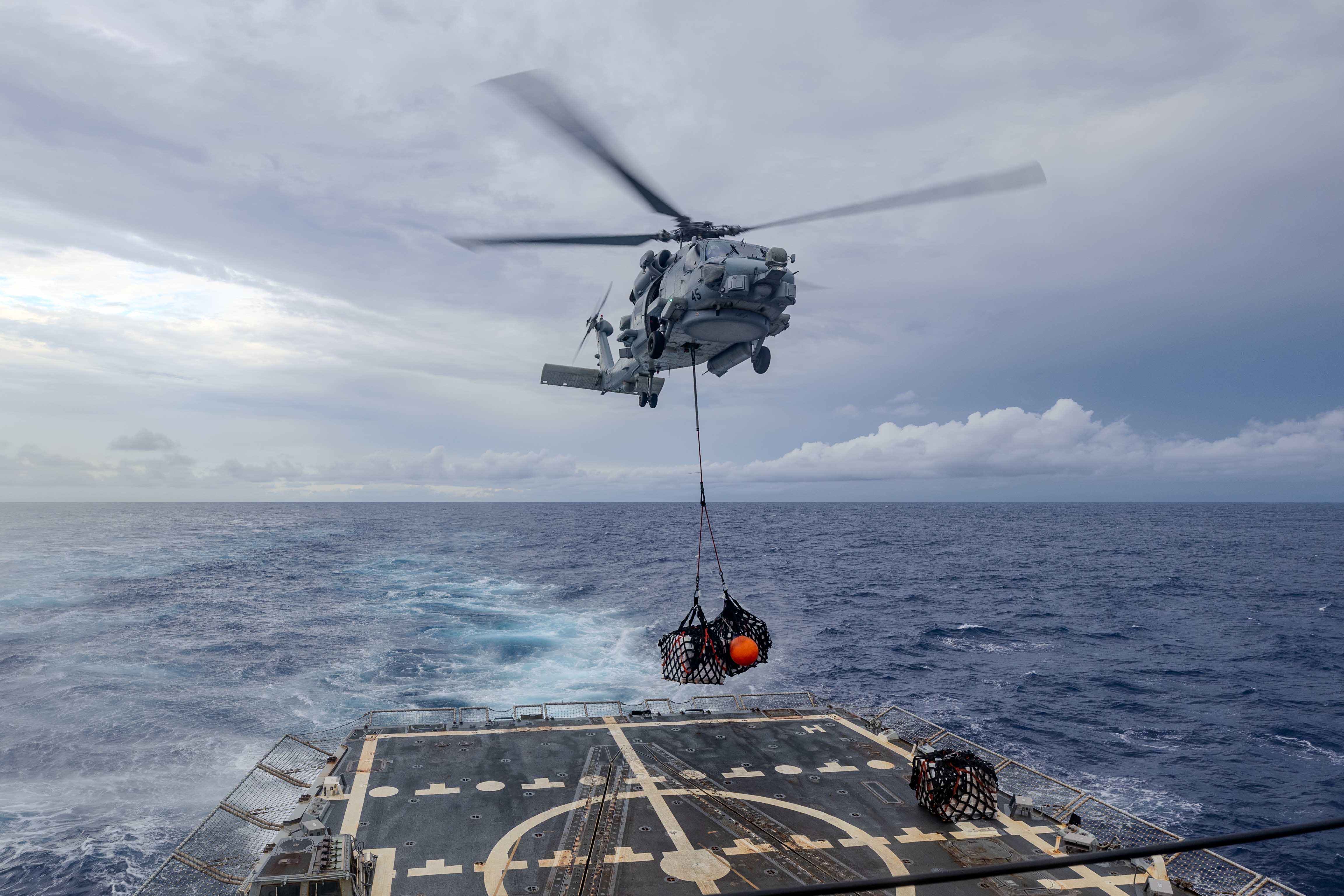 An MH-60R assigned to Helicopter Maritime Strike Squadron (HSM) 49 det. 4 the “High Rollers” carries pallets to the flight deck of the Arleigh Burke-class guided-missile destroyer USS Ralph Johnson (DDG 114) during a vertical replenishment (VERTREP) with the Lewis and Clark-class dry cargo and ammunition ship USNS Cesar Chavez (T-AKE 14) while underway in the Indian Ocean, April 26.