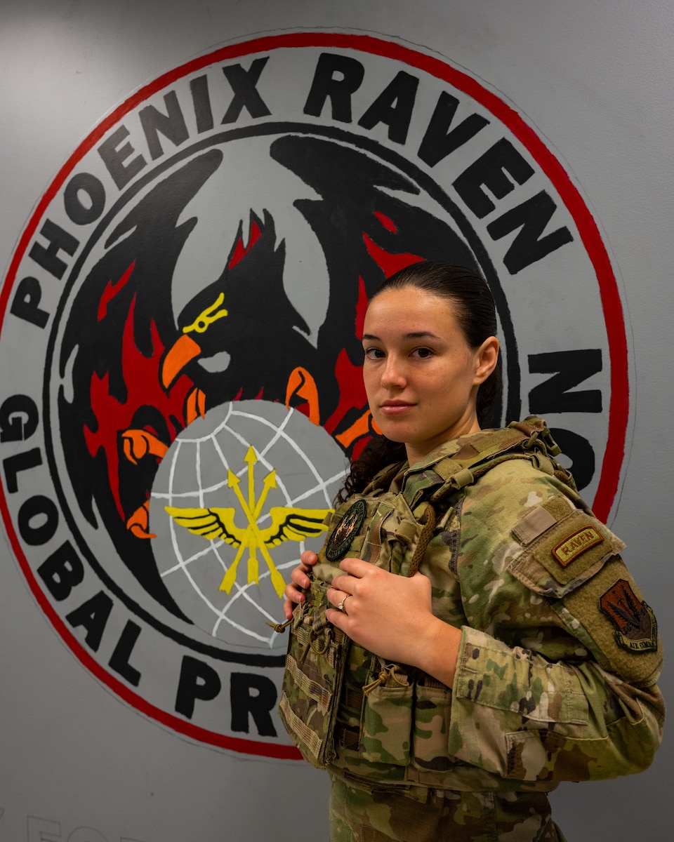 Senior Airman Alexa Reeves poses for a photo in front of a Phoenix Raven patch painting on a wall.