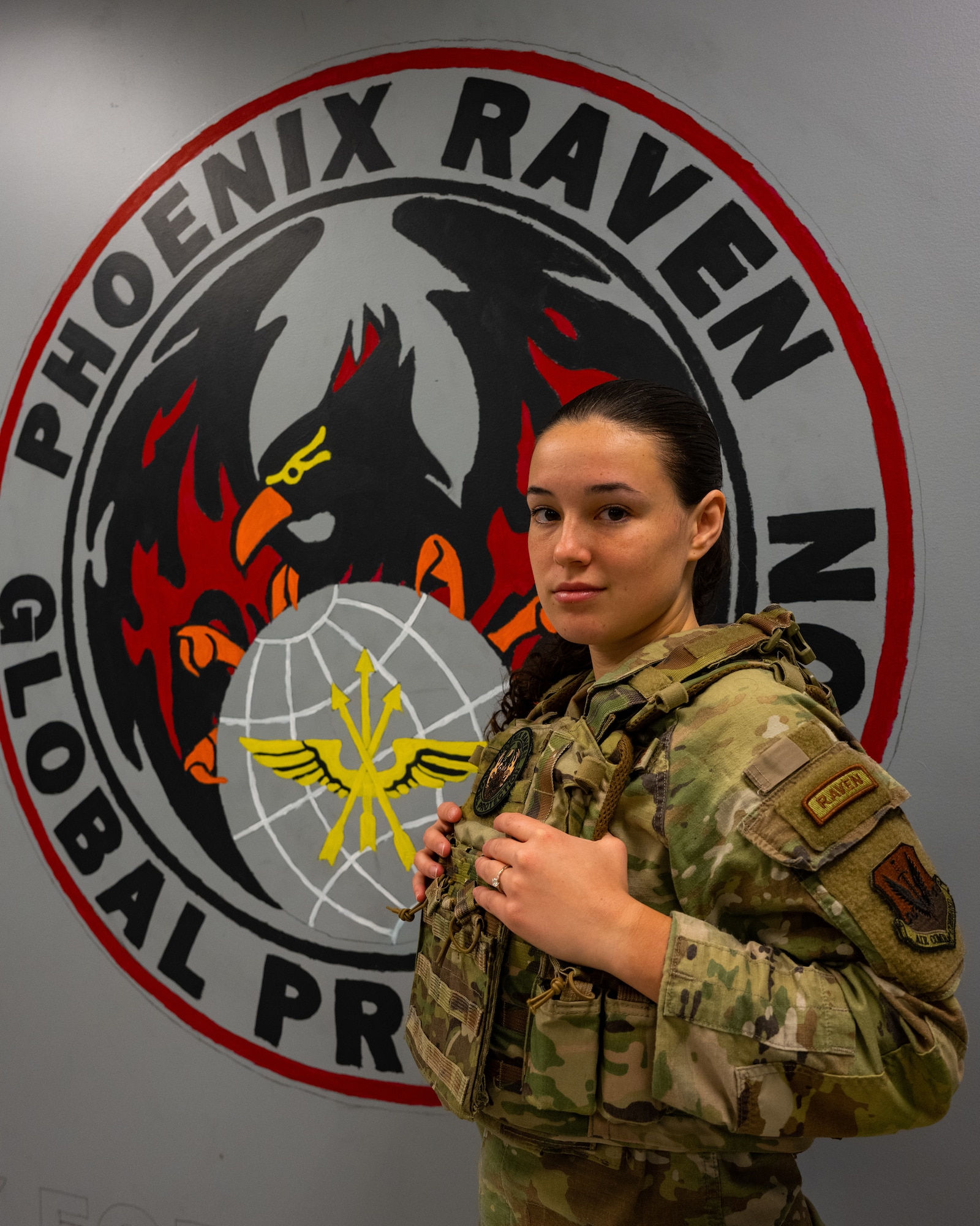 Senior Airman Alexa Reeves poses for a photo in front of a Phoenix Raven patch painting on a wall.