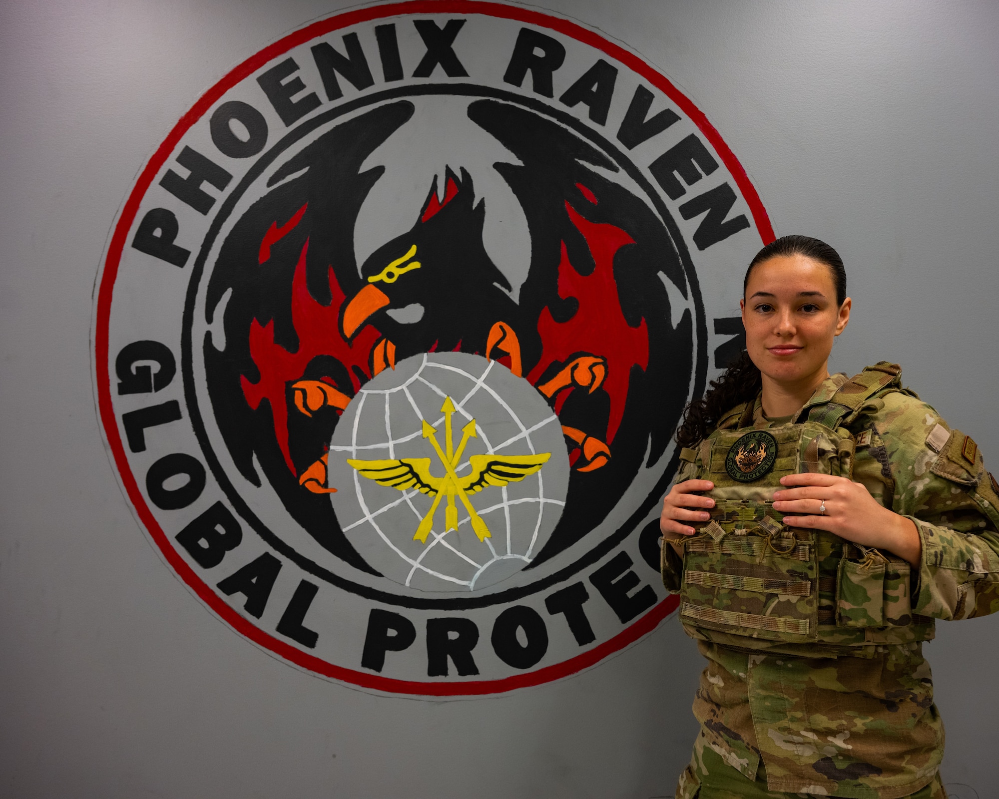Senior Airman Alexa Reeves poses for a photo in front of a Phoenix Raven patch painting on a wall.
