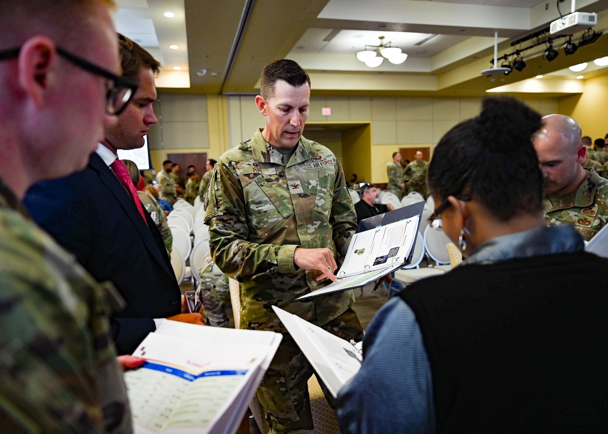 Judging panel stands in a group, holding binders, discussing and selecting the winning idea during Keesler AFB's Dragon Tank Event.