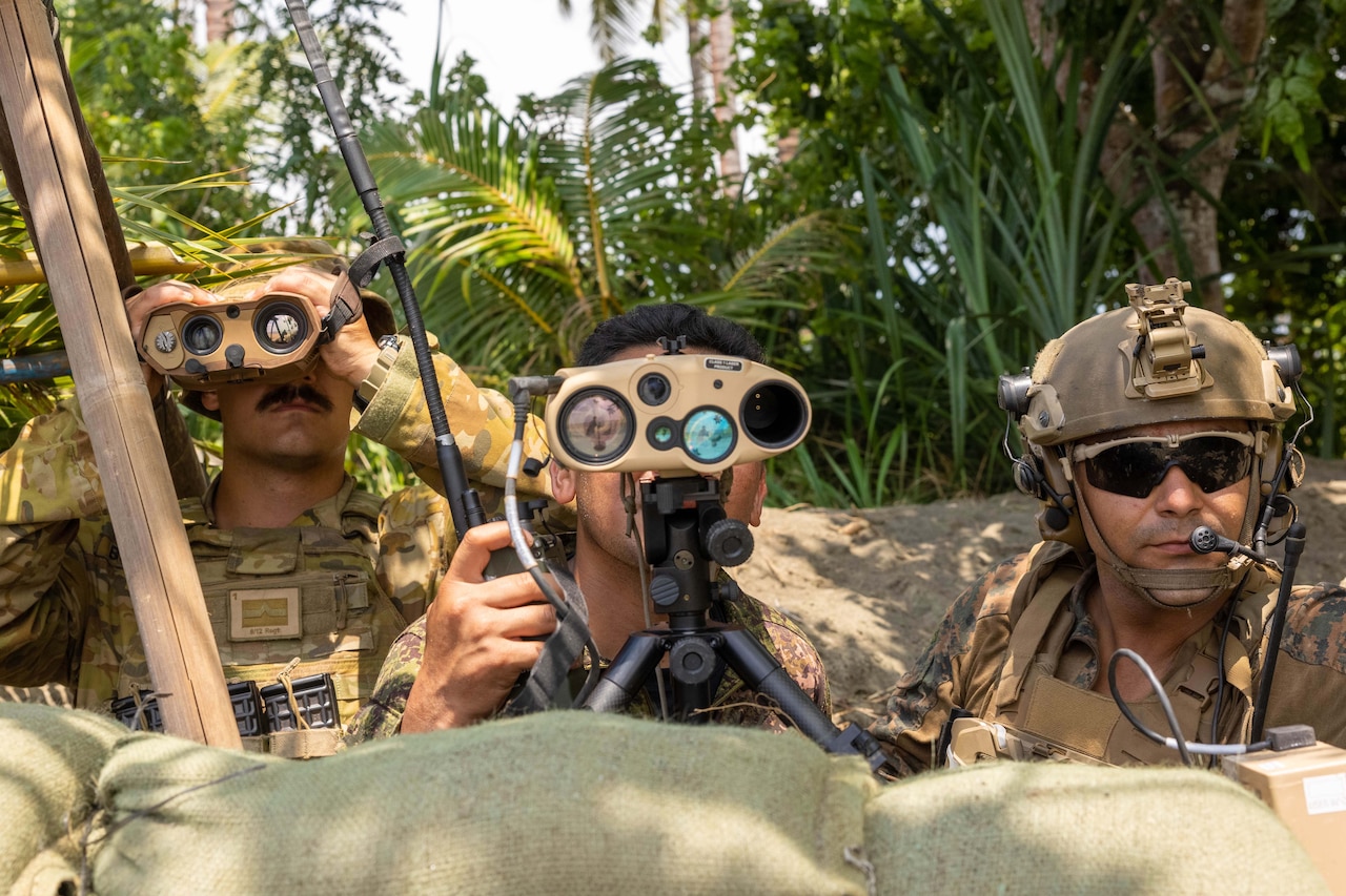 A Marine, a soldier and an airman sit in a tropical setting, while two use binoculars.