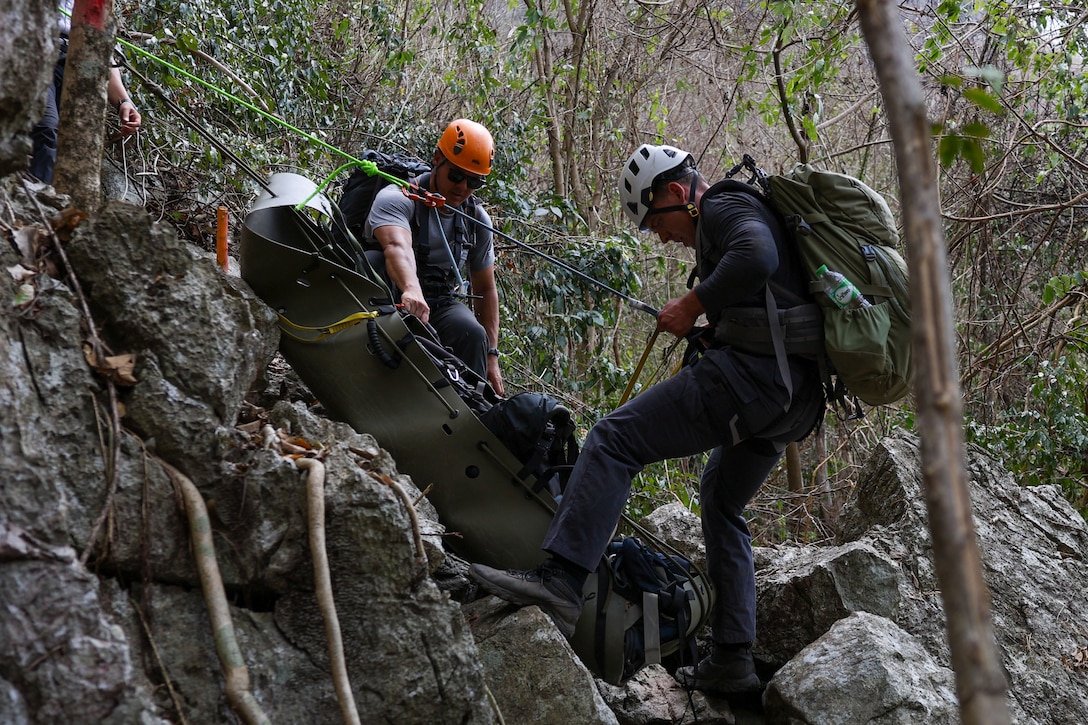 U.S. Army Staff Sgt. Danny Black, left, a team sergeant and U.S. Navy Hospital Corpsman 2nd Class Connor Dougherty, a medic, both with Defense POW/MIA Accounting Agency, lower a Skedco stretcher for a medical evacuation rehearsal during a recovery mission in Laos, Mar. 2, 2025.