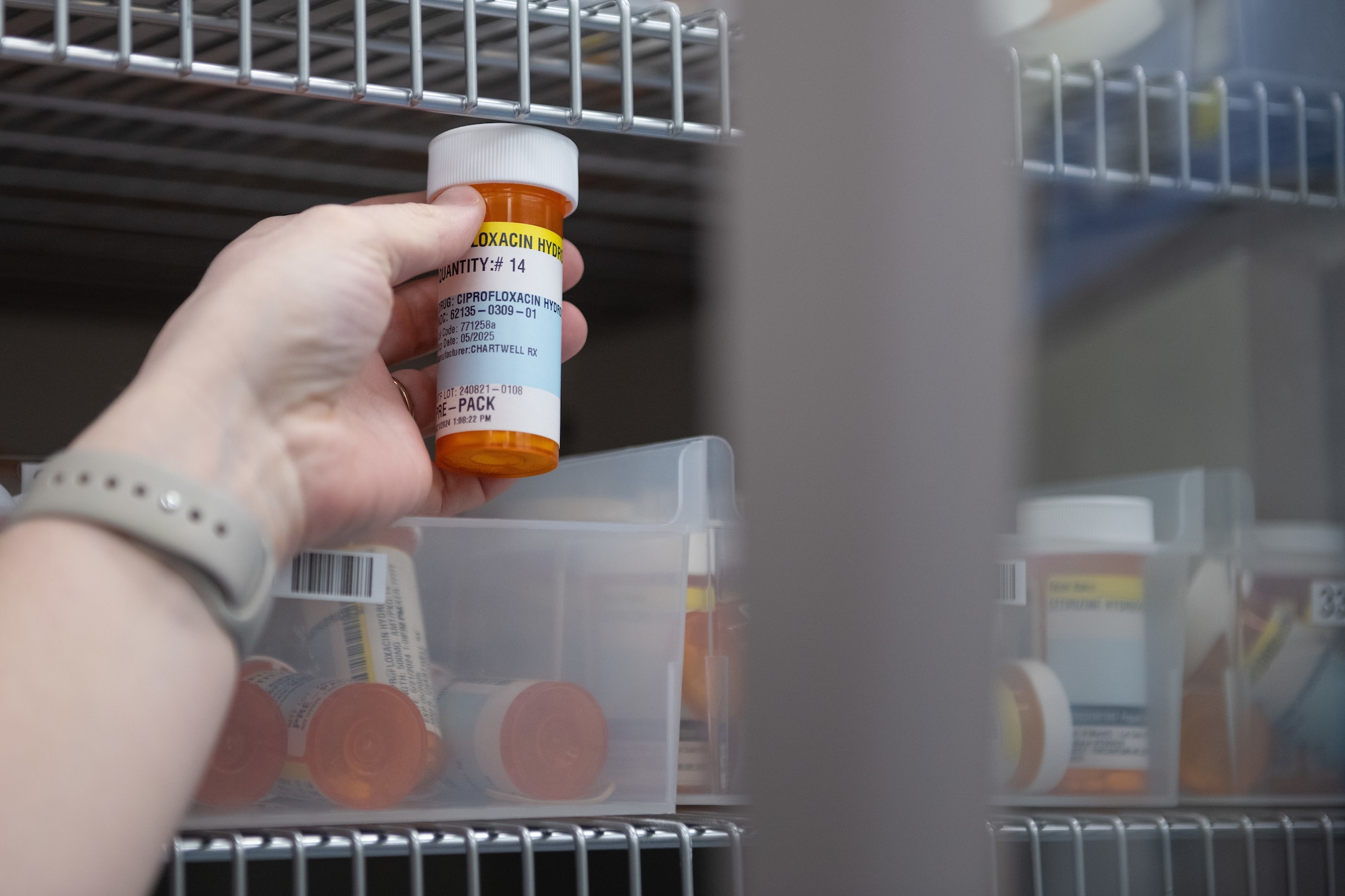 An Airman's hand is shown grabbing an orange medication bottle.