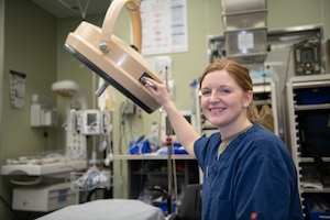 An  Airman wearing blue medical scrubs poses for a photo while holding onto medical equipment.