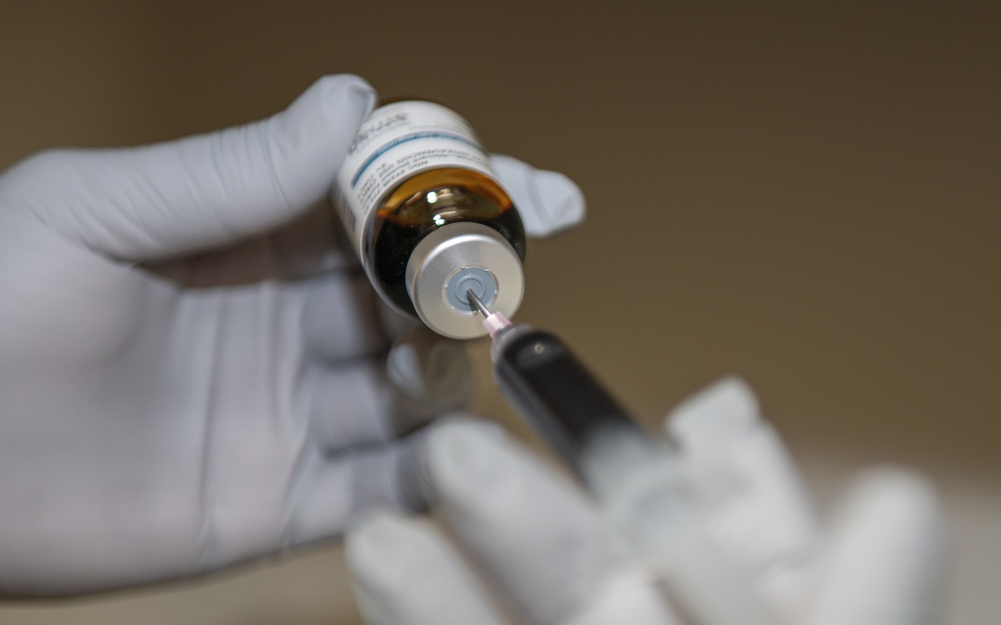 A hand inserts a needle into an IV medication bottle.