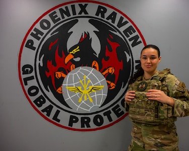 Senior Airman Alexa Reeves poses for a photo in front of a Phoenix Raven patch painting on a wall.