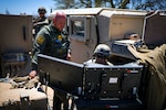 A soldier and a U.S. Border Patrol agent look at monitors during daylight.