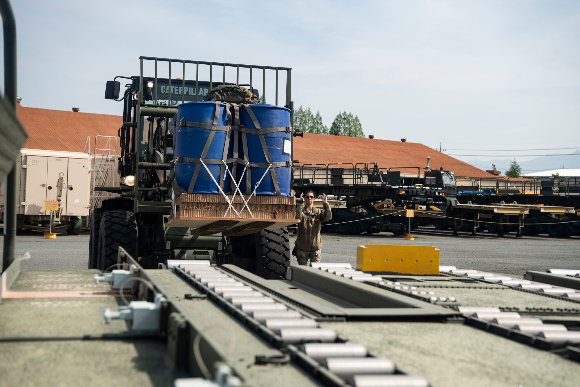 A forklift carrying two blue drums that are secured by netting