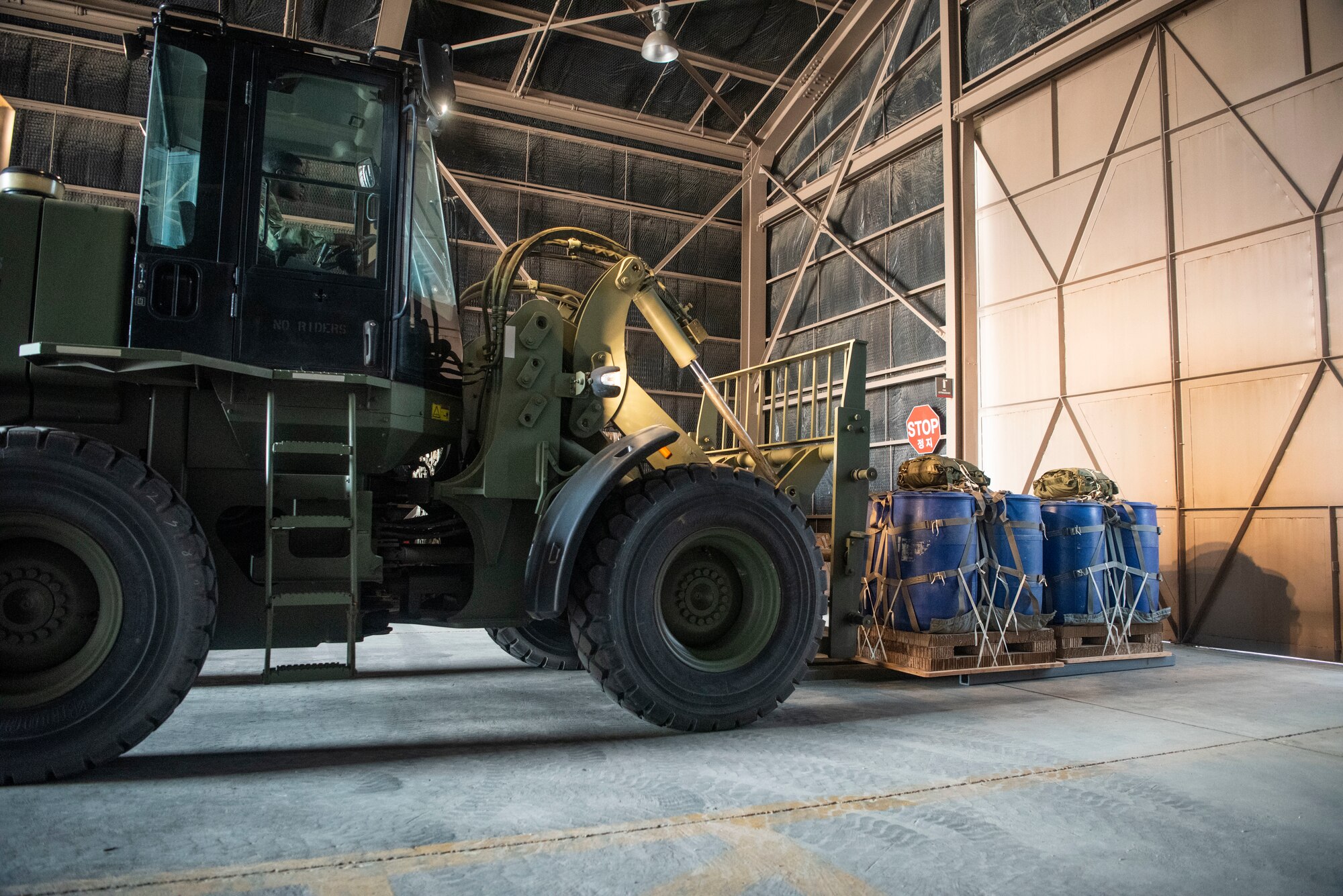A forklift picks up a pallet of blue drums secured by cargo netting