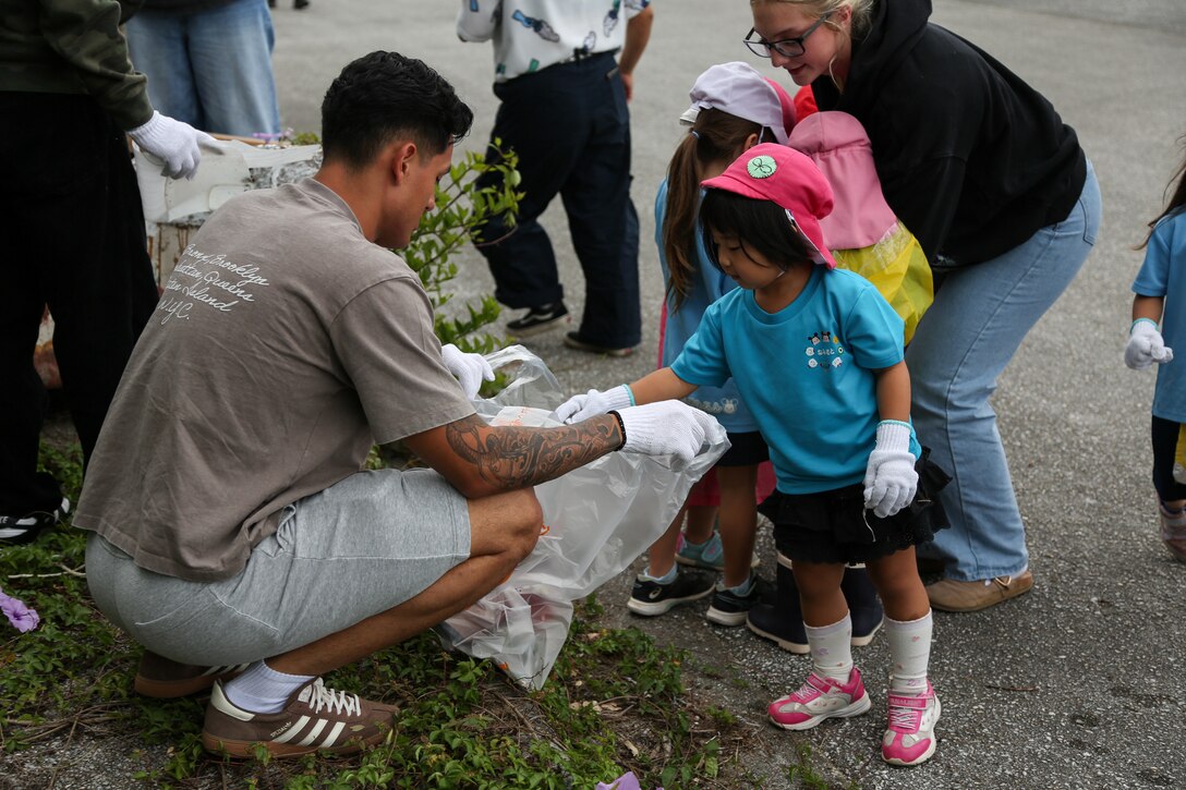 U.S. Marine Corps Cpl. Andres Hernandez, an infantryman with 12th Littoral Combat Team, 12th Marine Littoral Regiment, 3d Marine Division, holds a trash bag for a local preschool student during an Earth Day cleanup and tree-planting event at Nature Mirai in Kin Town, Okinawa, Japan, April 25, 2025. Marine Corps Installations Pacific coordinated a week of Earth Day events to reinforce relationships between U.S. service members and the Okinawa community, and to preserve Okinawa’s environment. The volunteers were from the Camp Hansen Single Marine Program, Hamada Preschool, and Namisato Preschool. Hernandez is a native of New Jersey. (U.S. Marine Corps photo by Cpl. Jesse Davis)