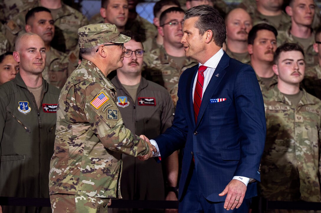 Defense Secretary Pete Hegseth shakes hands with an Army general as troops stand behind them.