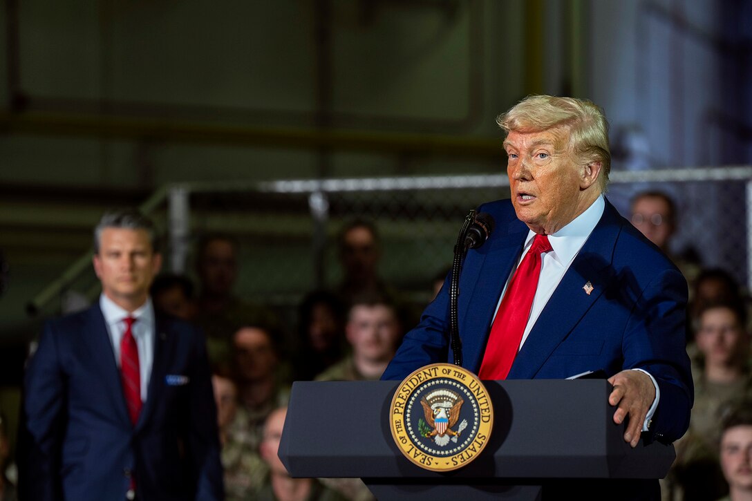 President Donald J. Trump speaks at a lectern as Defense Secretary Pete Hegseth and others listen.