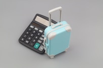 Calculator and travel suitcase on gray background