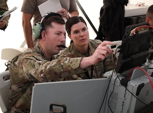 Tech. Sgt. Peyton Shaffer briefs Maj. Lauren Davis on mission threads during a vulnerability window, or vul, at Project Convergence Capstone 5 at the National Training Center, Fort Irwin, California, March 10, 2025. Shaffer, a weapons and tactics NCO with the 752nd Operational Support Squadron, is operating within the PC-C5 experiment. Davis, an air battle manager with the 224th Air Defense Sector supporting the ABMS Program Office, is evaluating the functionality of the Tactical Operations Center-Light system. (Official Air Force Photo by Morgan Brown)