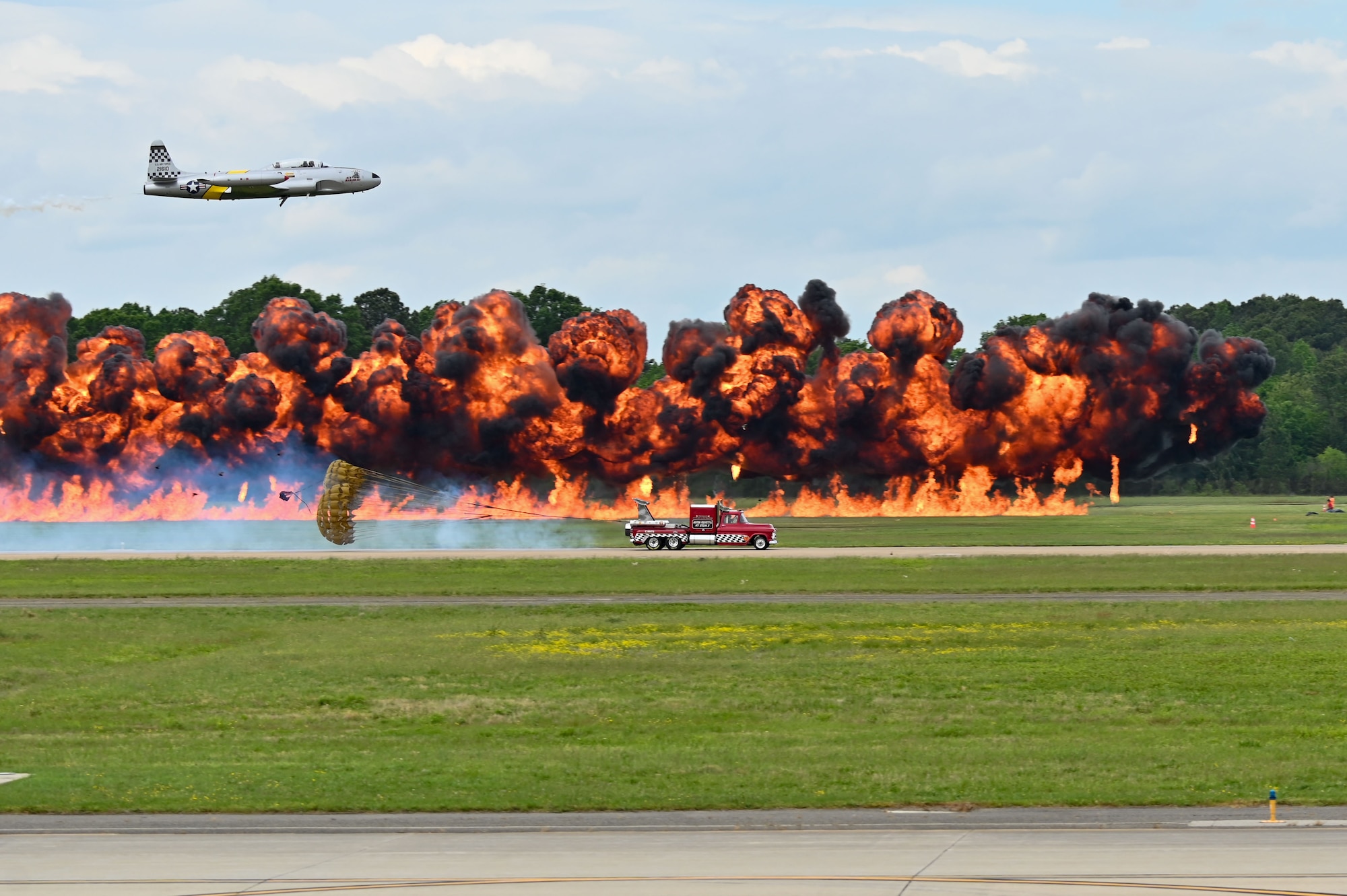 A truck and a plane race in front of an explosion.
