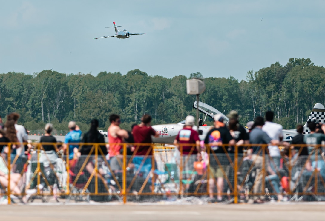 A plane passes low in front of a crowd.