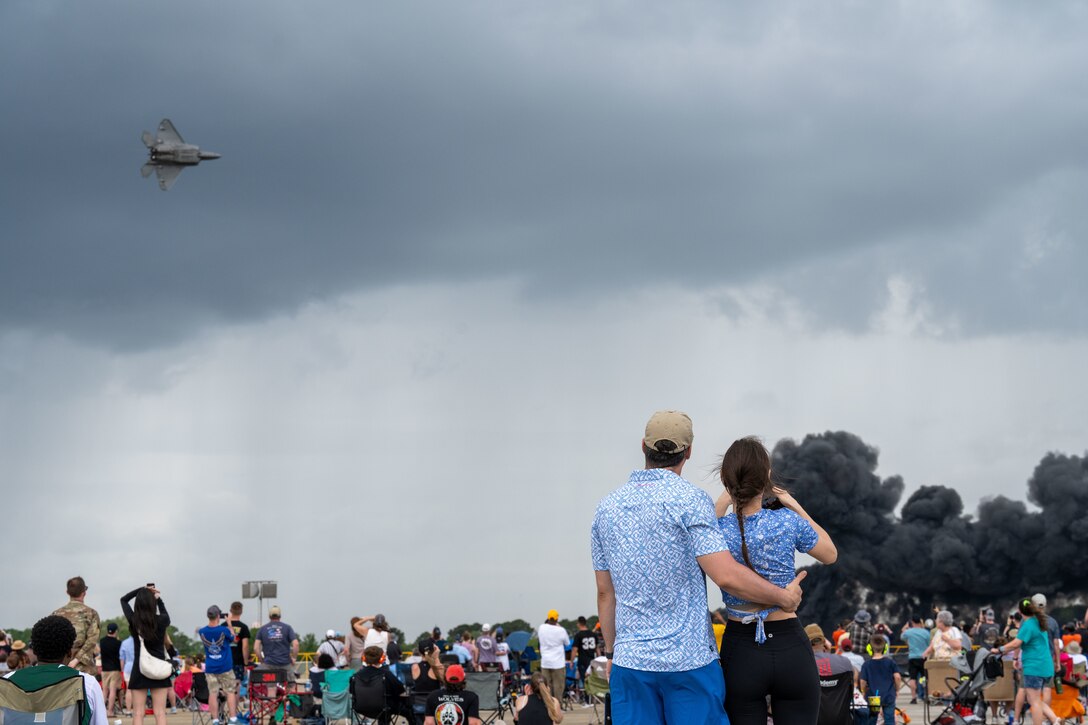 A crowd of people watch a plane fly.