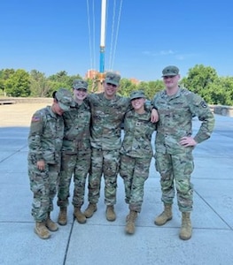 Five Soldiers in duty uniform pose for a photo outside.