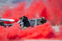 A photo of Airmen shooting through a cloud of red smoke