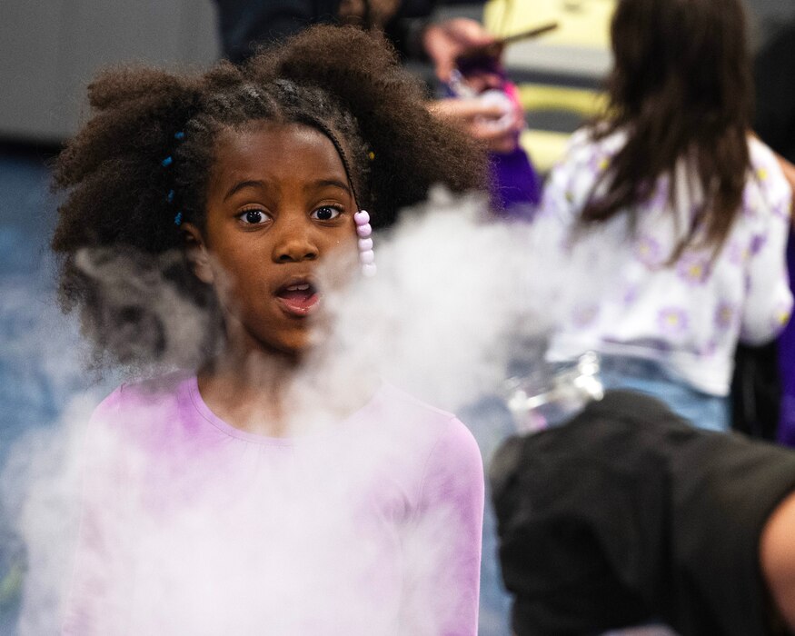 An African American girl stands with her mouth agape looking at a cloud of vaper.