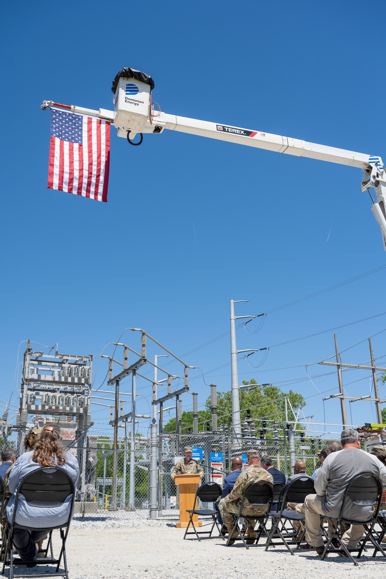 A man stands behind a podium speaking to a crowd under an American flag.