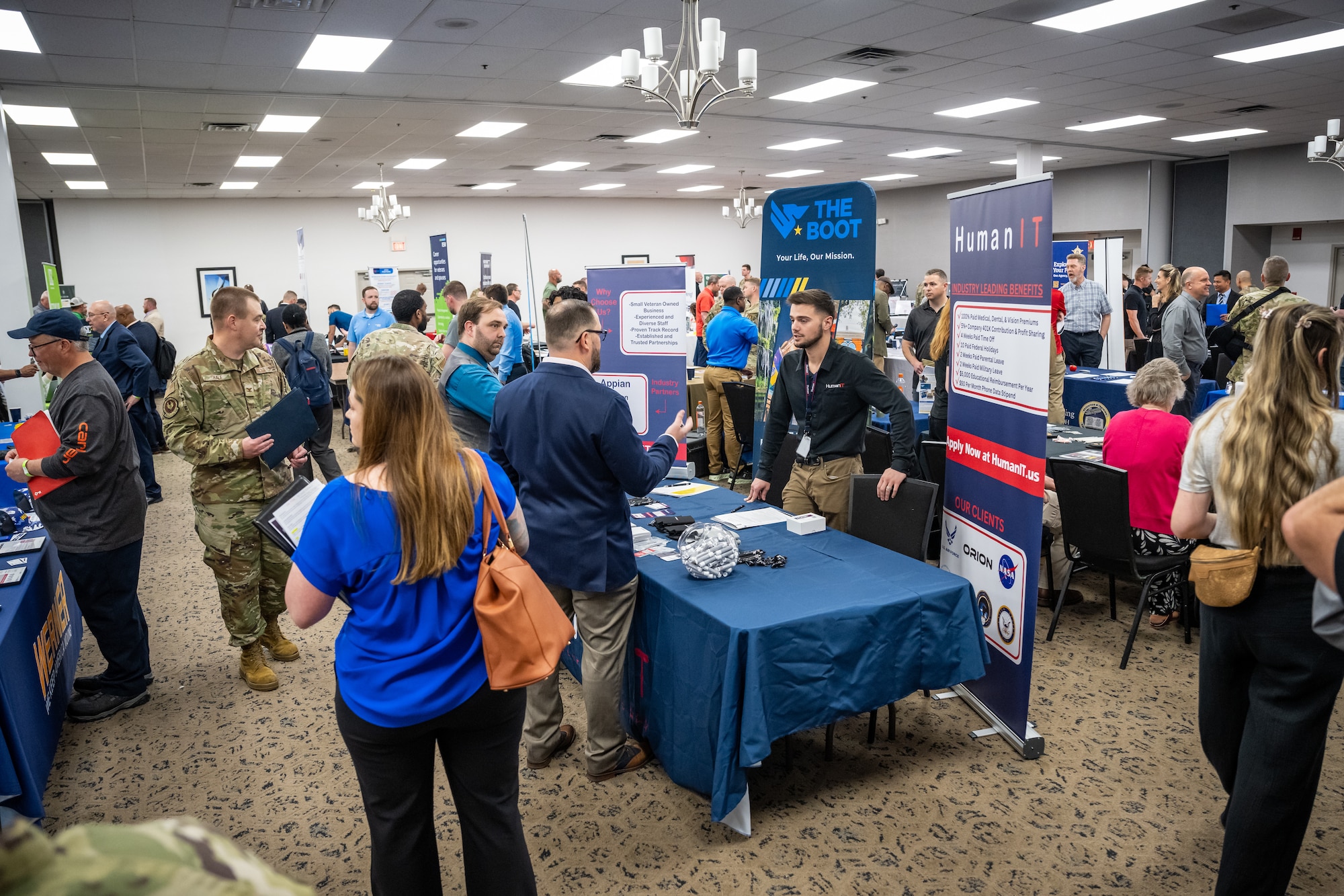 A wide view of a conference room filled with a variety of people, service members in uniform and business casual attire